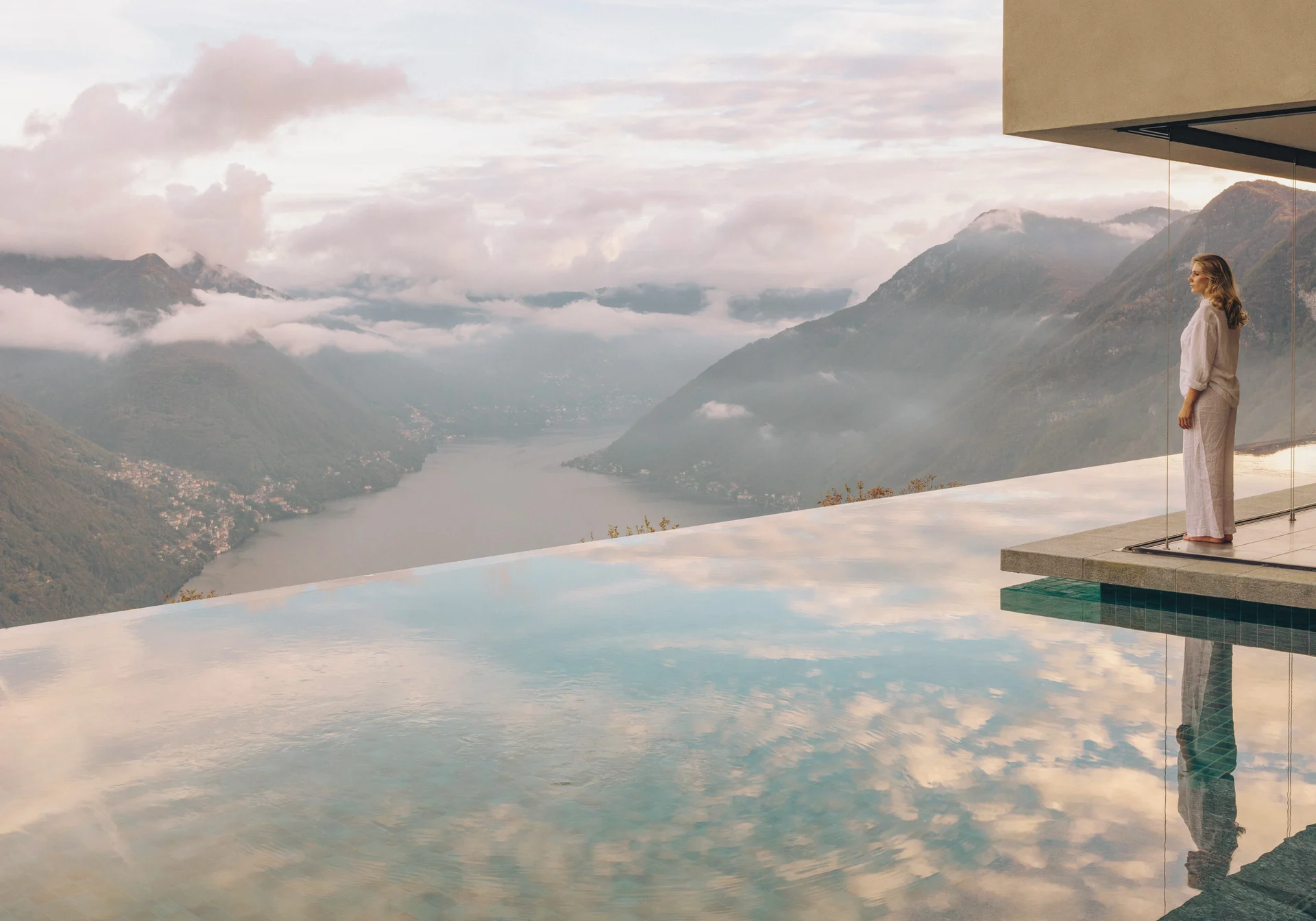 A guest looks out over a mountain lake from the edge of an infinity pool.